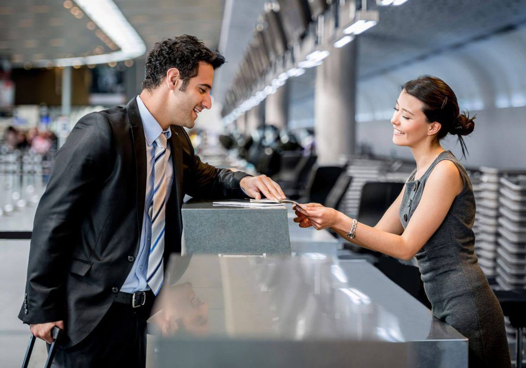 Man at airport check-in counter speaking with attendant across the desk