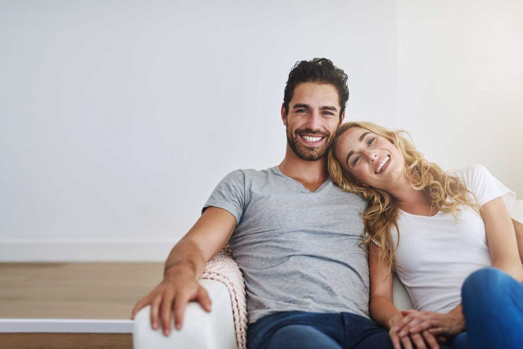 Smiling couple sitting on a couch, the woman leaning her head on the man’s shoulder.