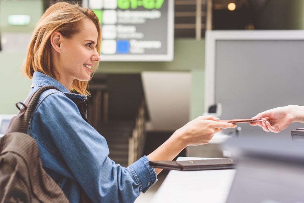 Woman at a counter handing a card to a cashier in a bright store checkout area
