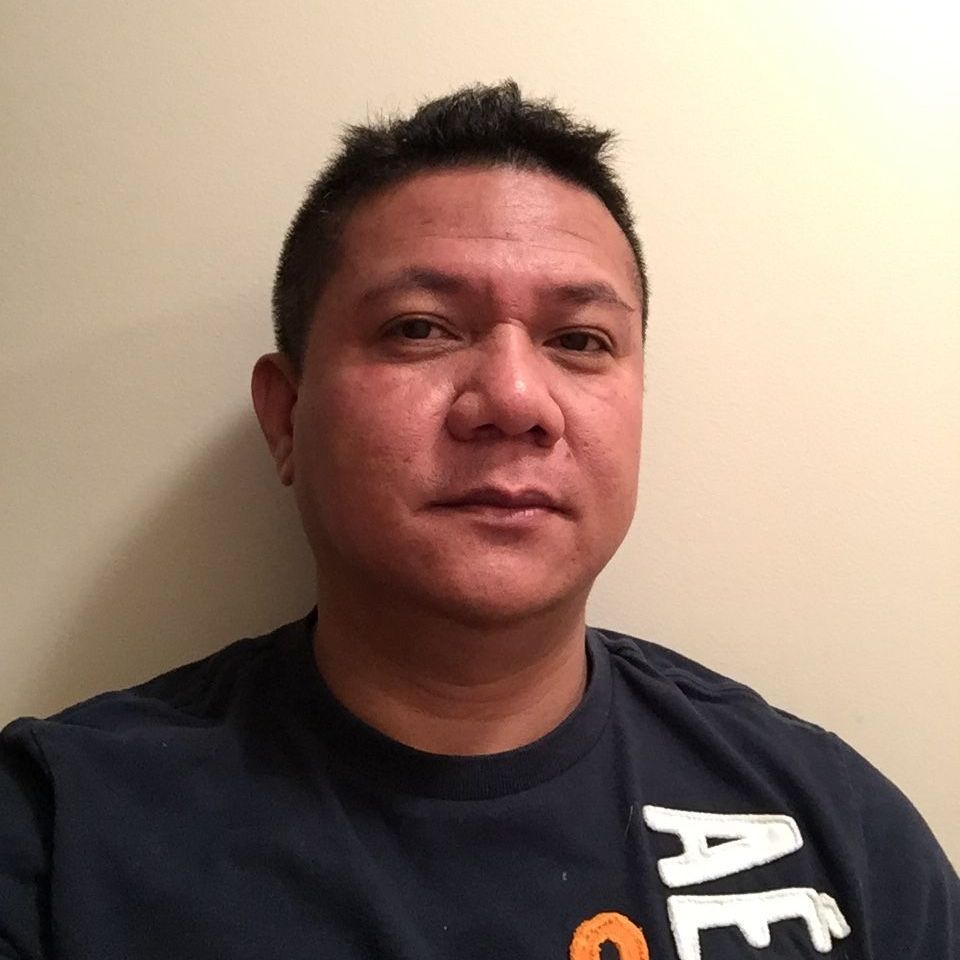 Portrait of a man in a dark shirt against a plain beige wall