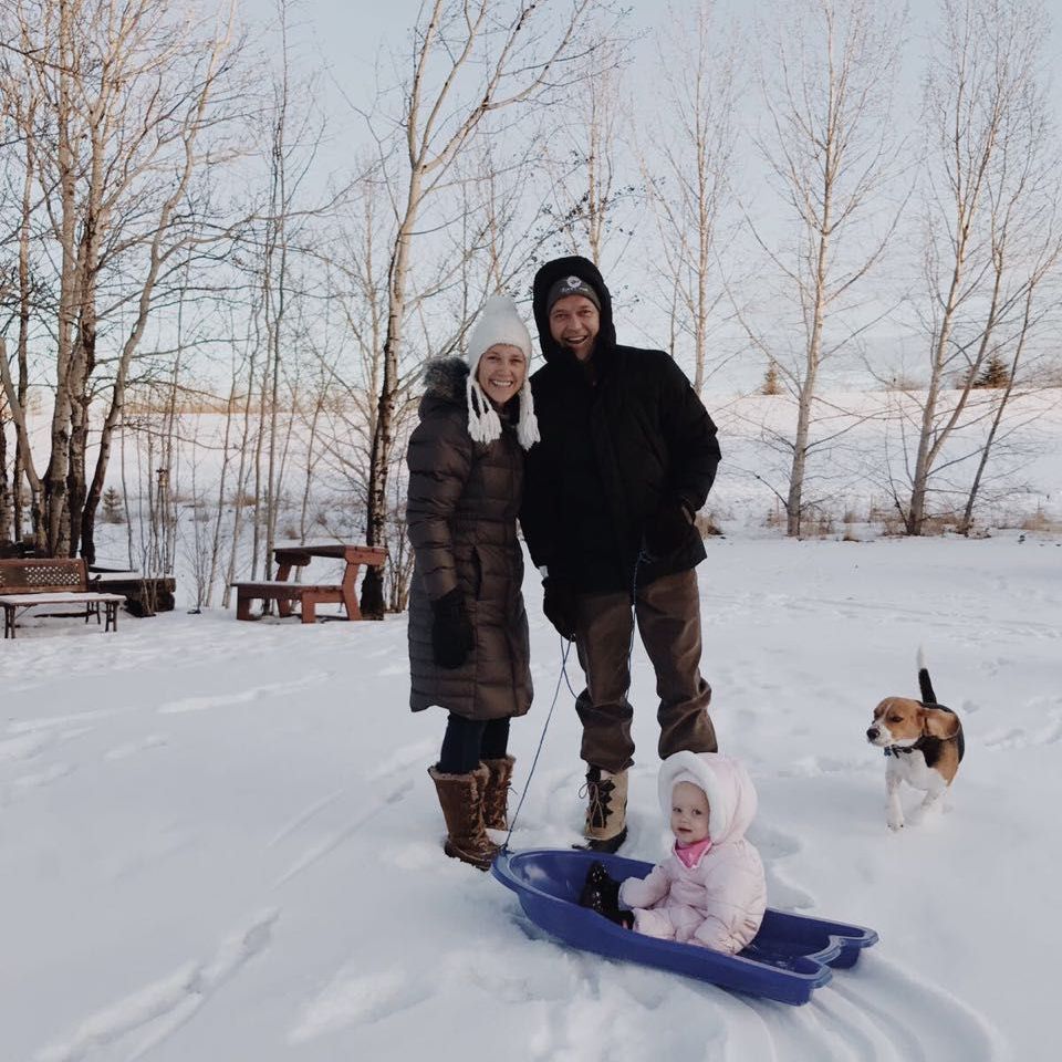 Family in winter snow with a child on a blue sled and a dog nearby.
