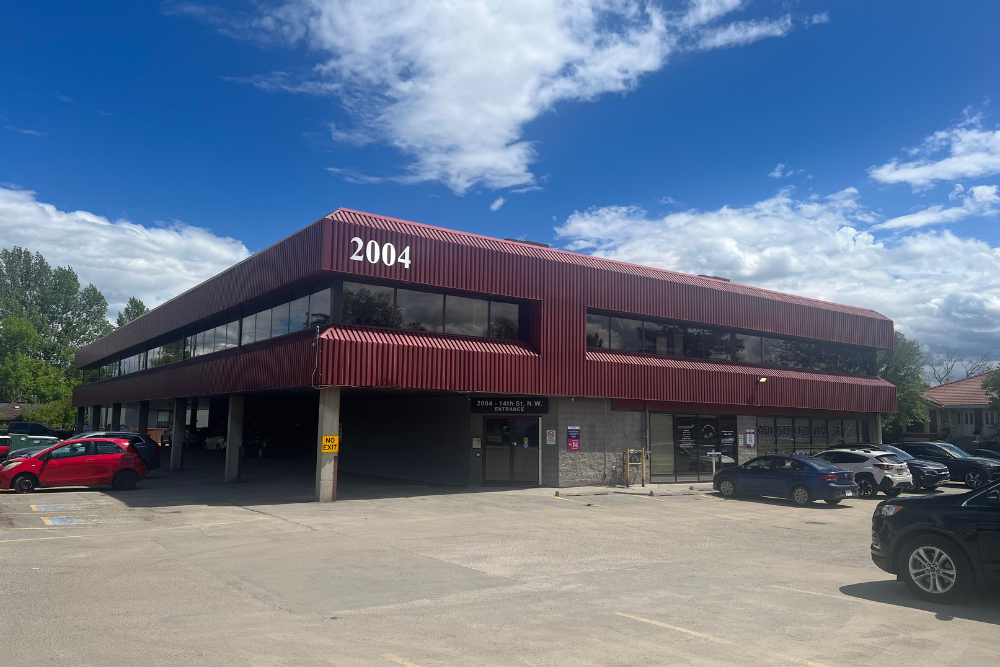 Two-story maroon office building with parking lot and trees under a blue sky, number 2104 visible on the facade