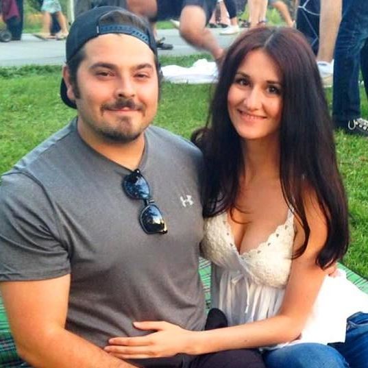 Smiling couple sitting on grass outdoors, with the woman hugging the man.