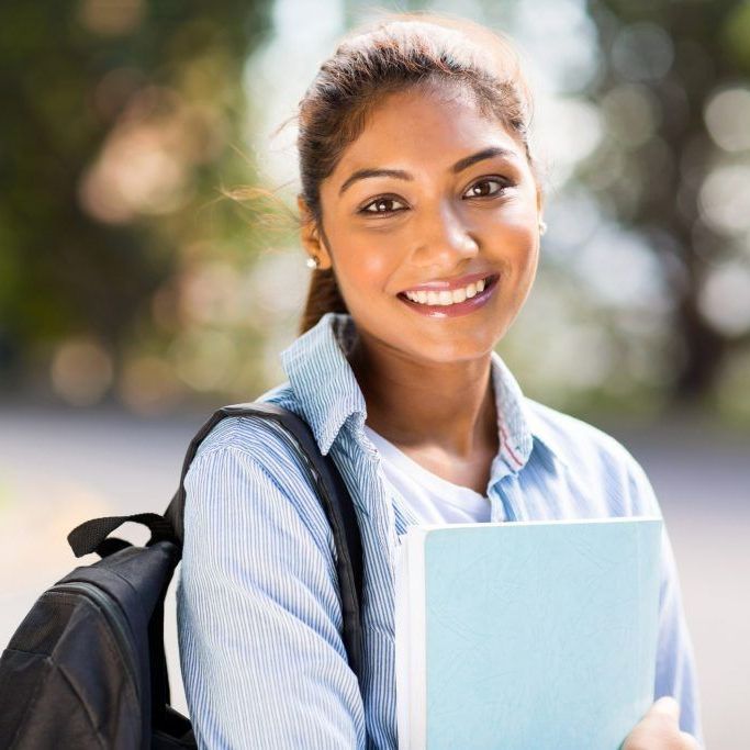 Smiling student with backpack holding a light blue notebook outdoors