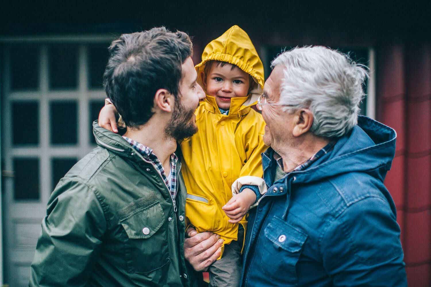 Two adults smiling at a child in a yellow raincoat outdoors in front of a building