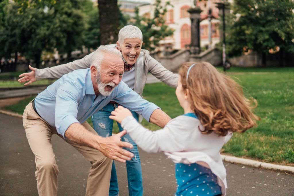 Three people hugging and laughing on a park path outdoors, with trees and grass in the background