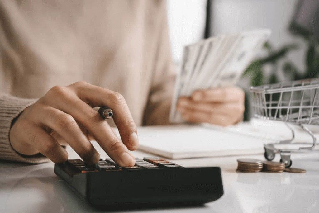 Hand using a calculator beside papers and coins on a desk
