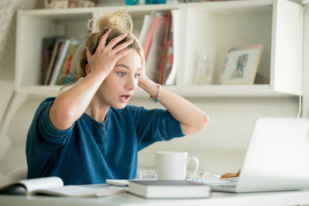 Person at a desk with laptop, hands on head, looking stressed in a bright home office
