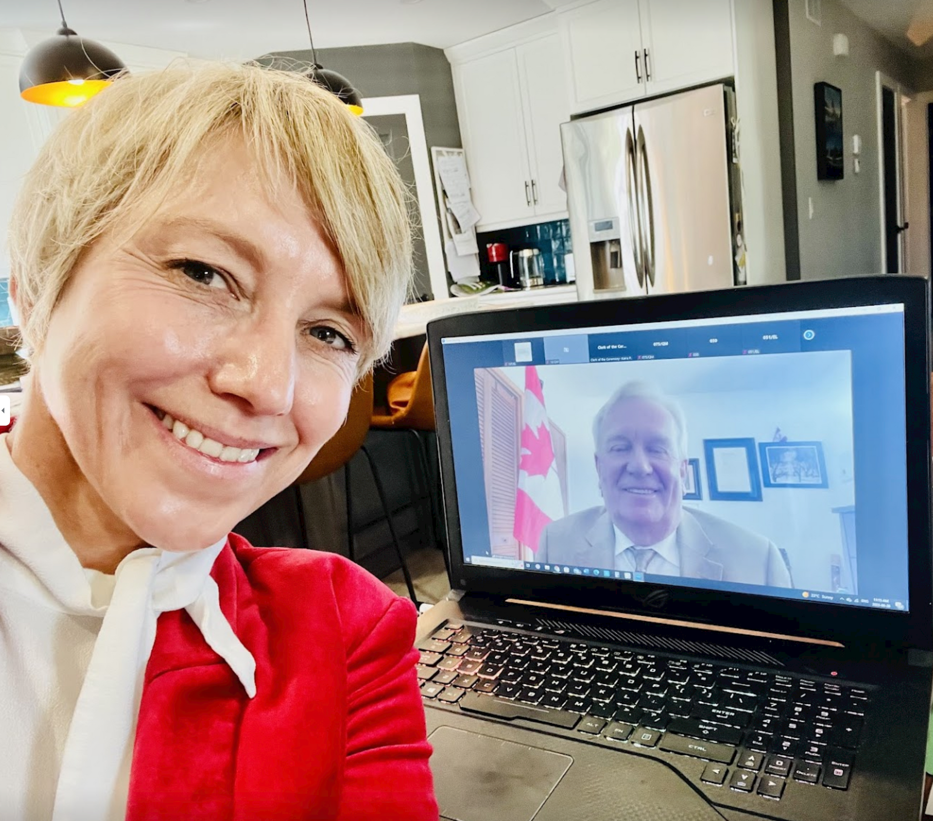 Person smiling beside laptop showing a video call with an older man in an office-like kitchen setting