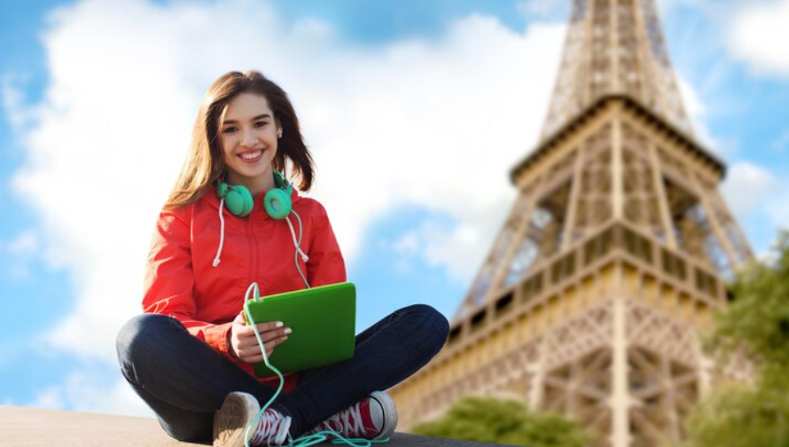 Woman with green headphones and laptop sitting in front of the Eiffel Tower on a sunny day