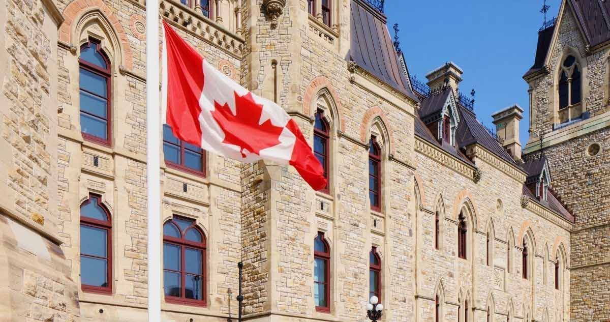 Stone building with arched windows and a large Canadian flag against a blue sky