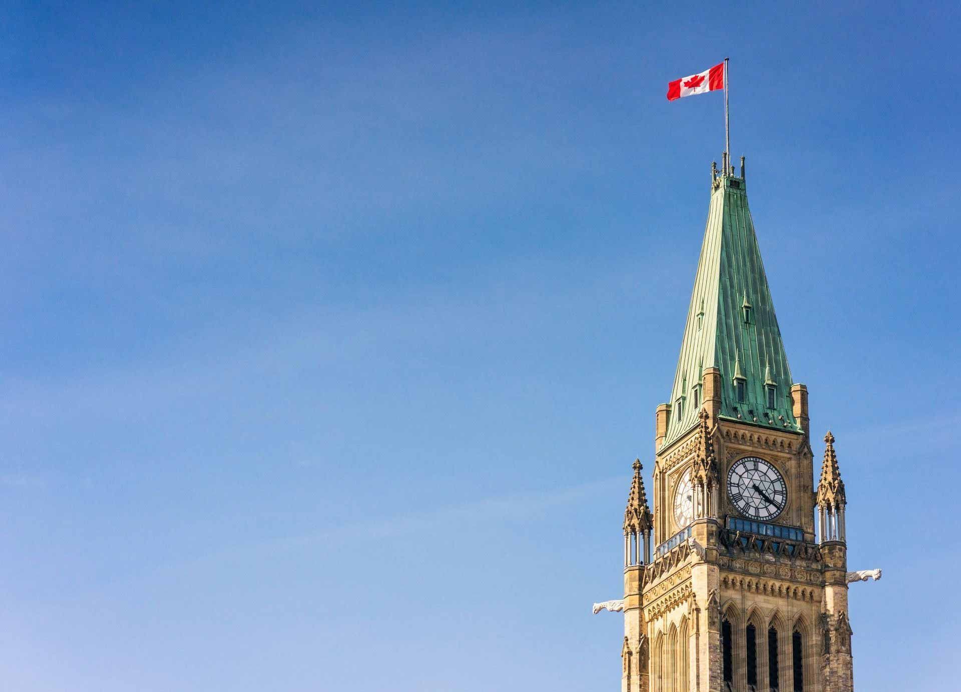 Parliament tower with a Canadian flag waving against a clear blue sky