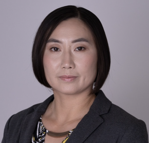 Studio headshot of a person in a dark blazer against a light gray background.