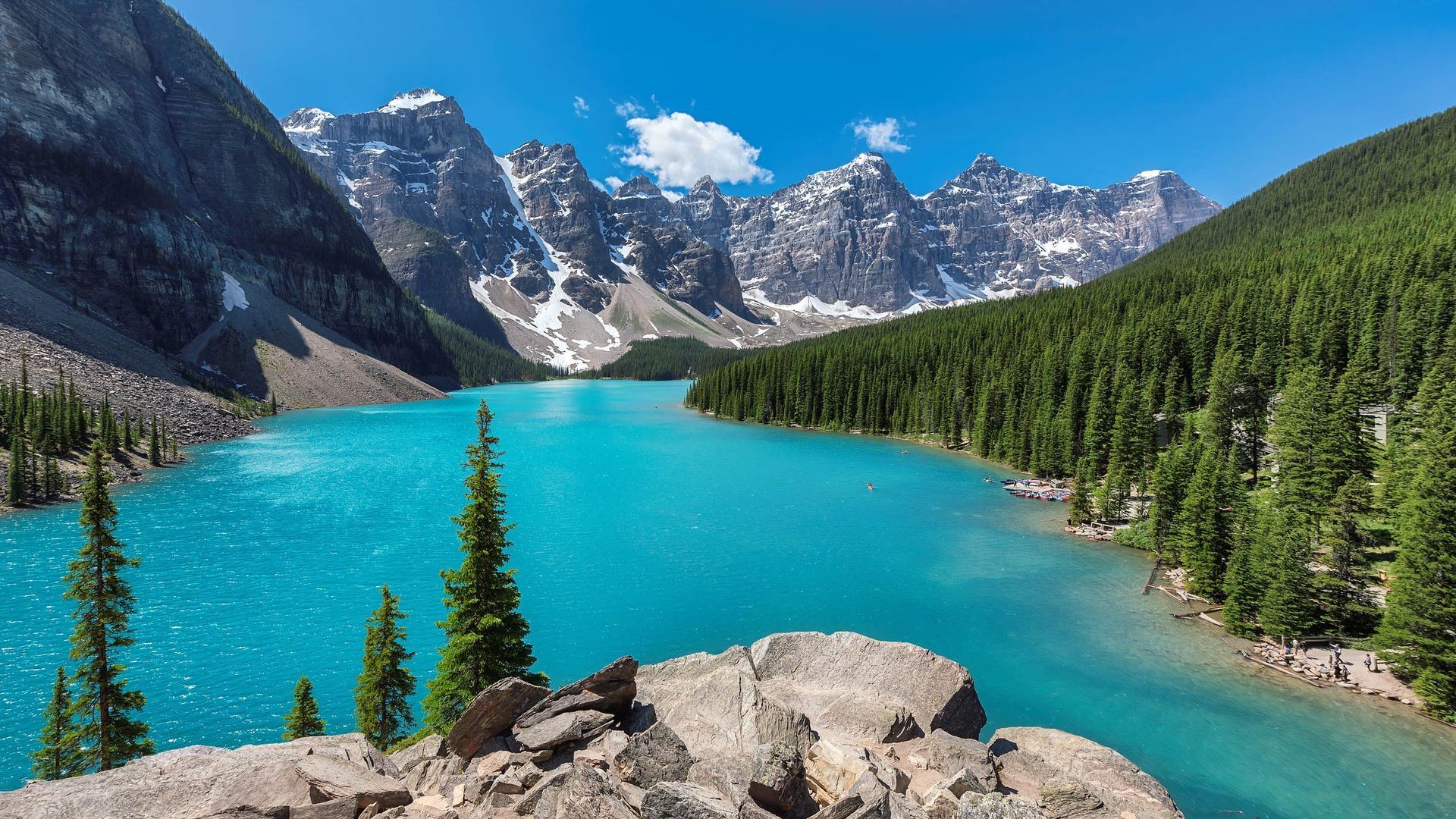 Turquoise alpine lake with pine trees and snowy mountains under a clear blue sky