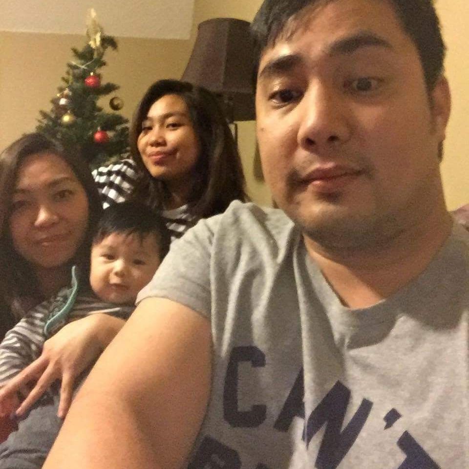 Family selfie on a couch in a living room, with a decorated Christmas tree in the background.