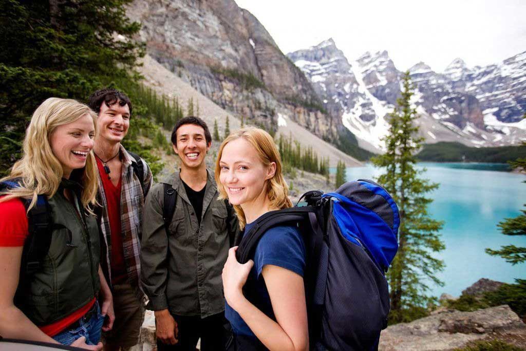Four hikers posing by a turquoise mountain lake with snowcapped peaks in the background