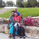 Four people smiling on a stone bench beside pink flowers in a park