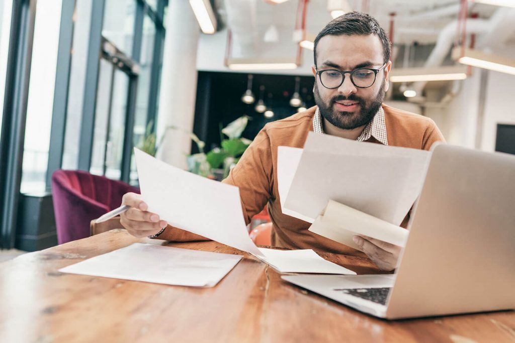 Person reviewing papers at a laptop in a bright office workspace