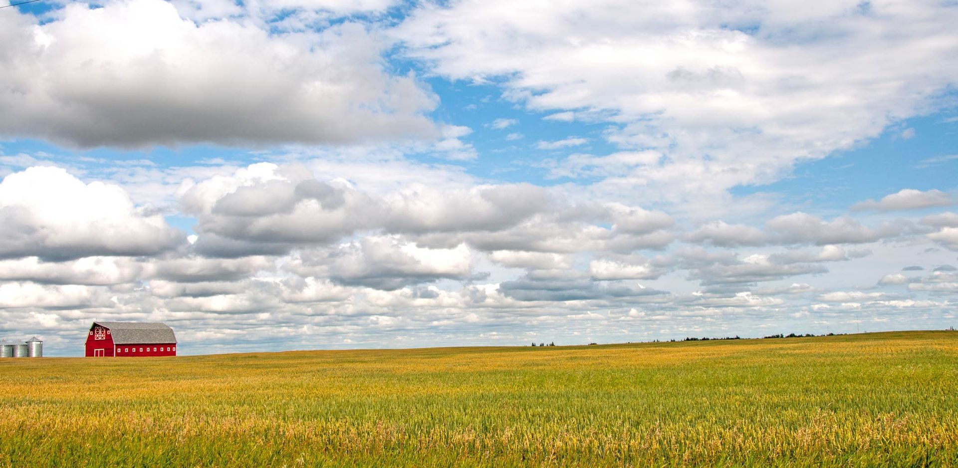 Red barn in a yellow-green field under a wide cloudy blue sky