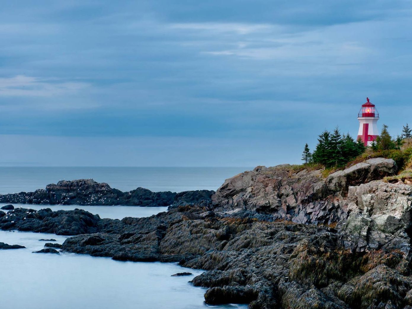 Rocky coastline with a red-and-white lighthouse under a cloudy blue sky