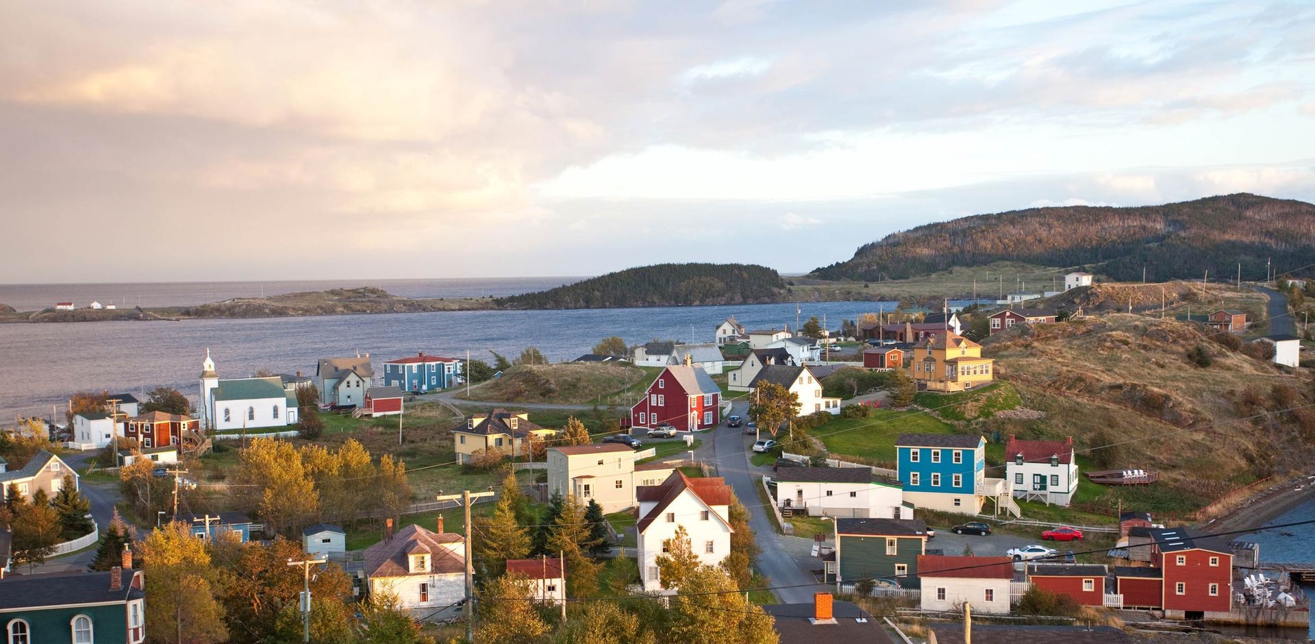 Coastal village with colorful houses overlooking a calm bay under a cloudy evening sky