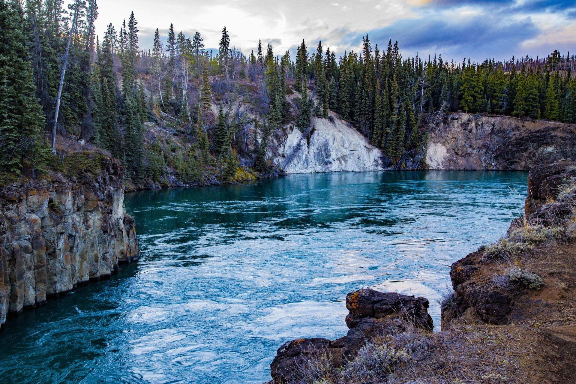 Turquoise river flowing through a rocky forest canyon under a cloudy sky