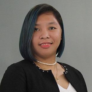 Portrait of a smiling person with short blue-black hair, wearing a black jacket and pearl necklace on a gray background