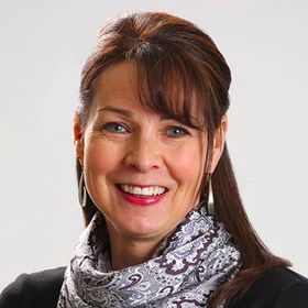 Smiling woman with brown hair and patterned scarf against a light background