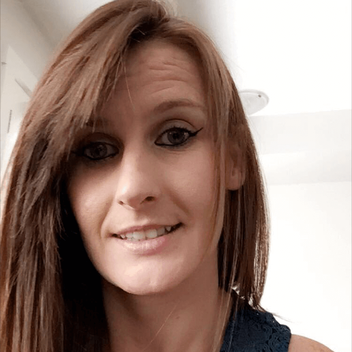 Portrait of a smiling person with brown hair and black eyeliner indoors