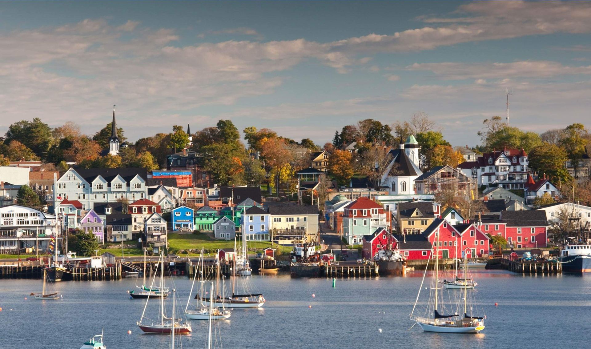 Colorful seaside village with sailboats on calm water and autumn trees along the shore