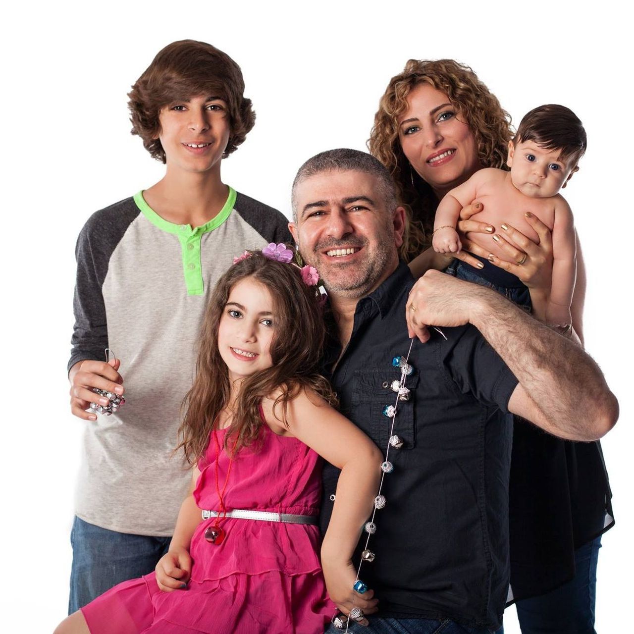 Family group portrait on a white background, with four adults and a baby smiling together