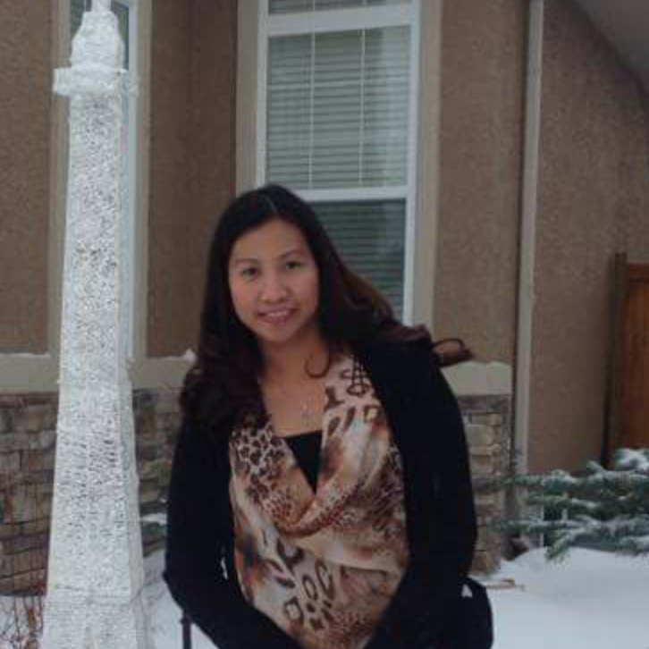 Woman smiling outdoors in a snowy yard, wearing a black coat and patterned scarf.