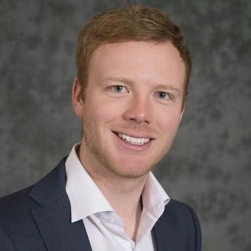 Smiling man in a navy suit and white shirt against a gray studio background
