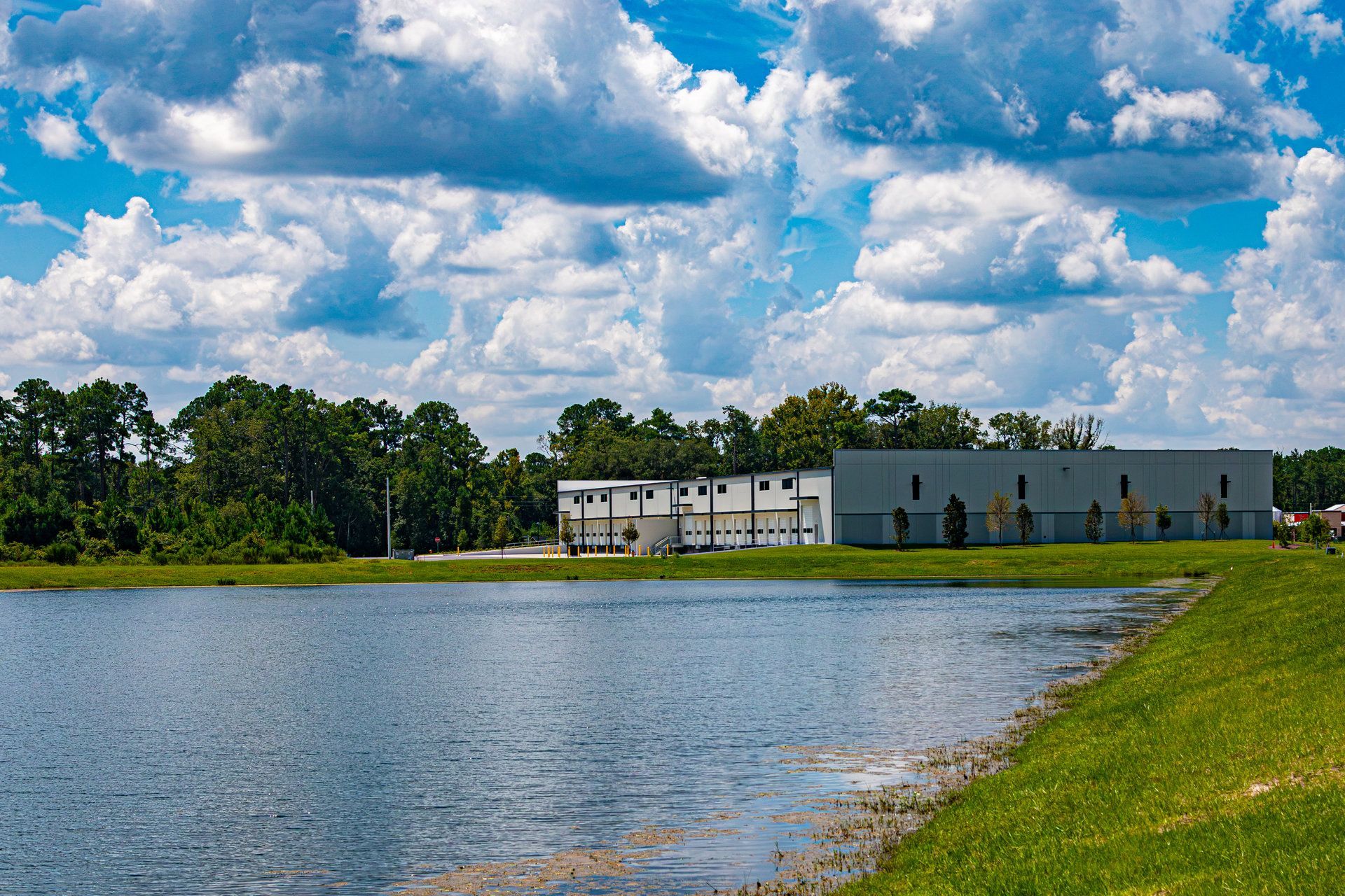 Lake along a grassy shore under a blue sky in Yulee, Florida, with pine trees and a building in the distance