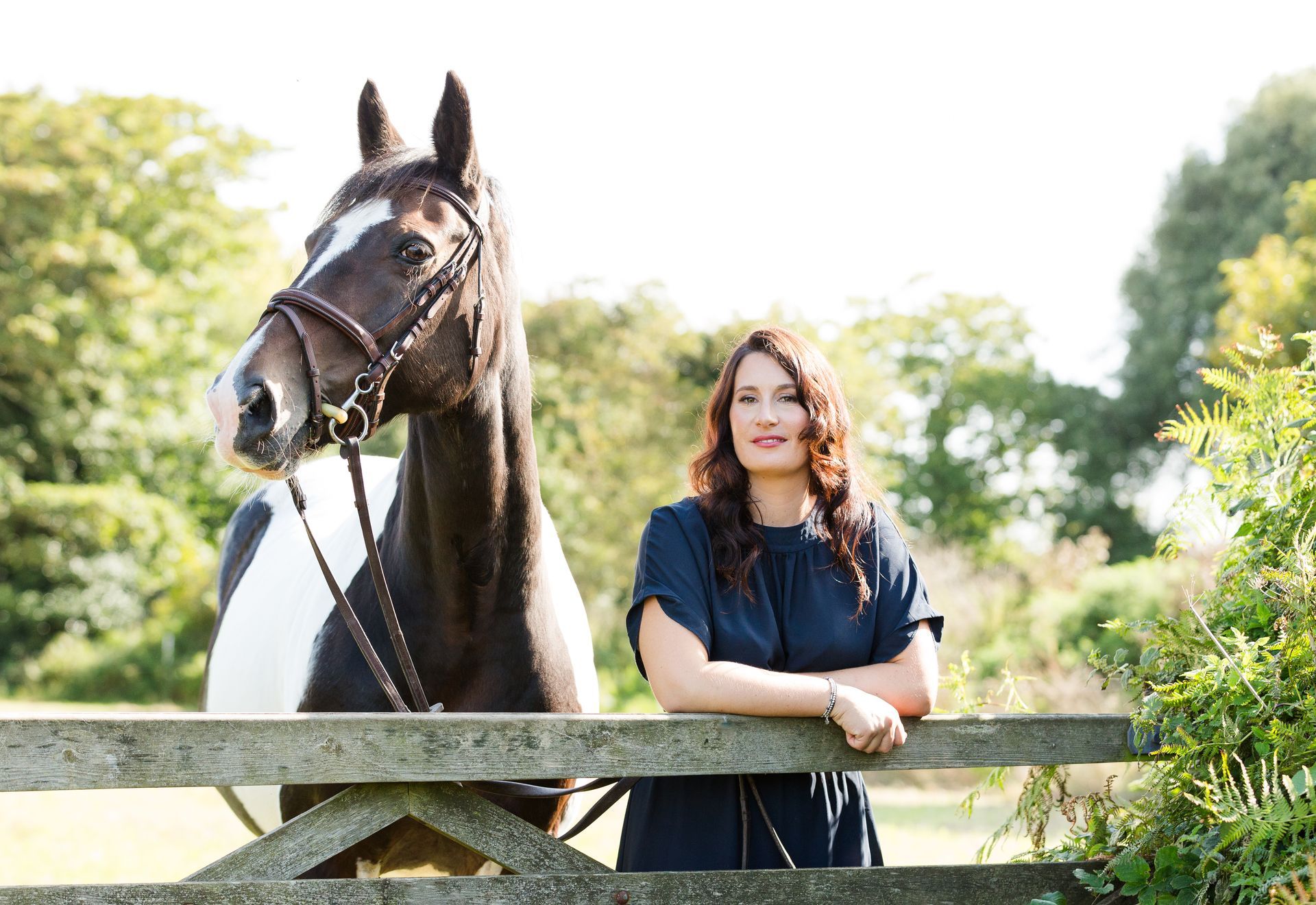 Woman in dark top, leaning on wooden fence with black and white horse. Outdoors.