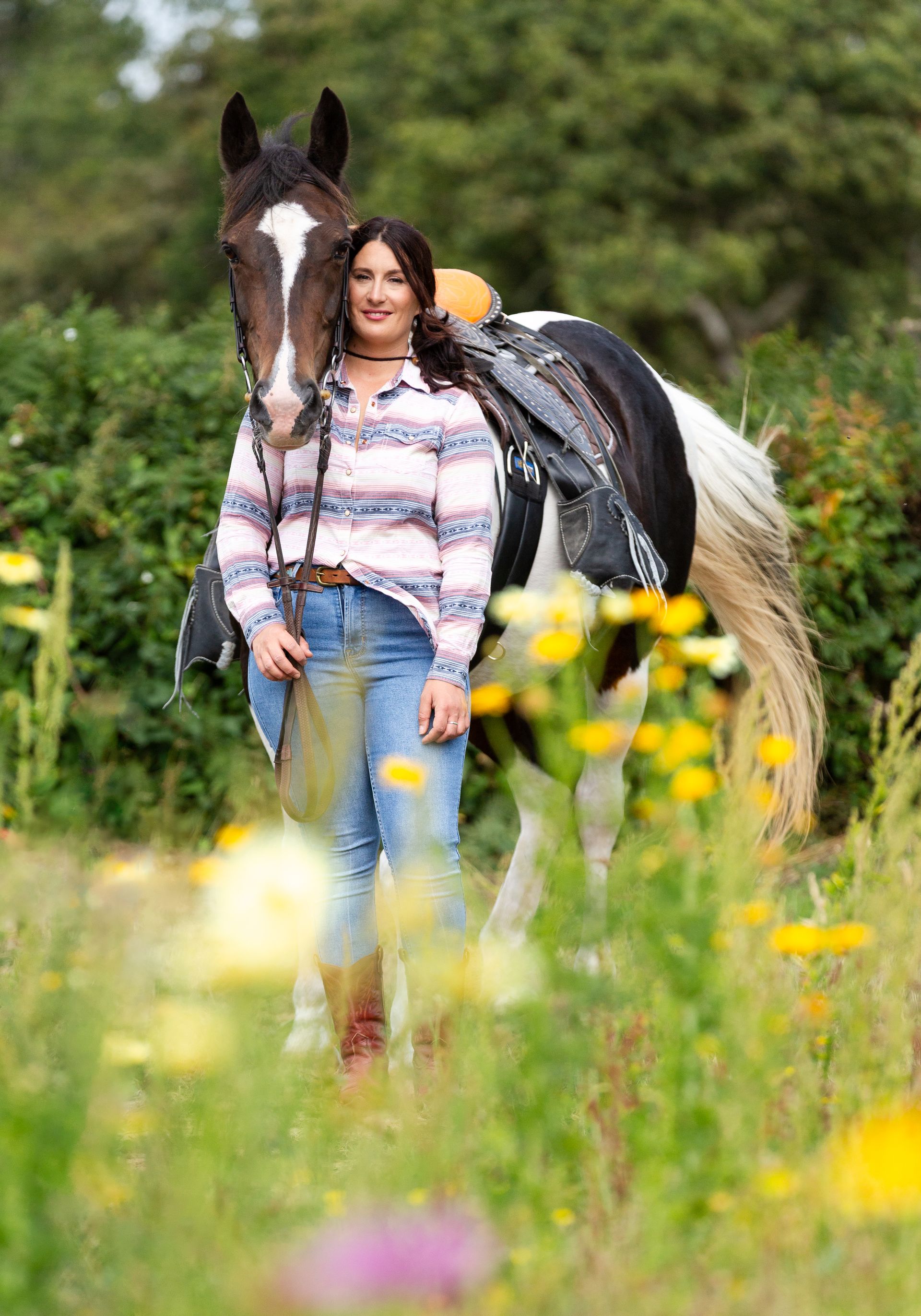 Woman standing with a paint horse in a field of wildflowers.