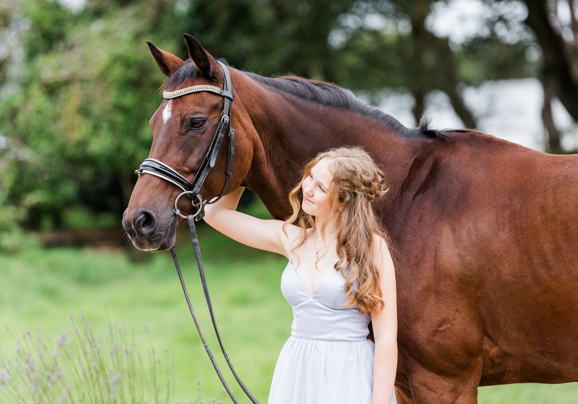 Woman in sparkly dress with a brown horse in a field.