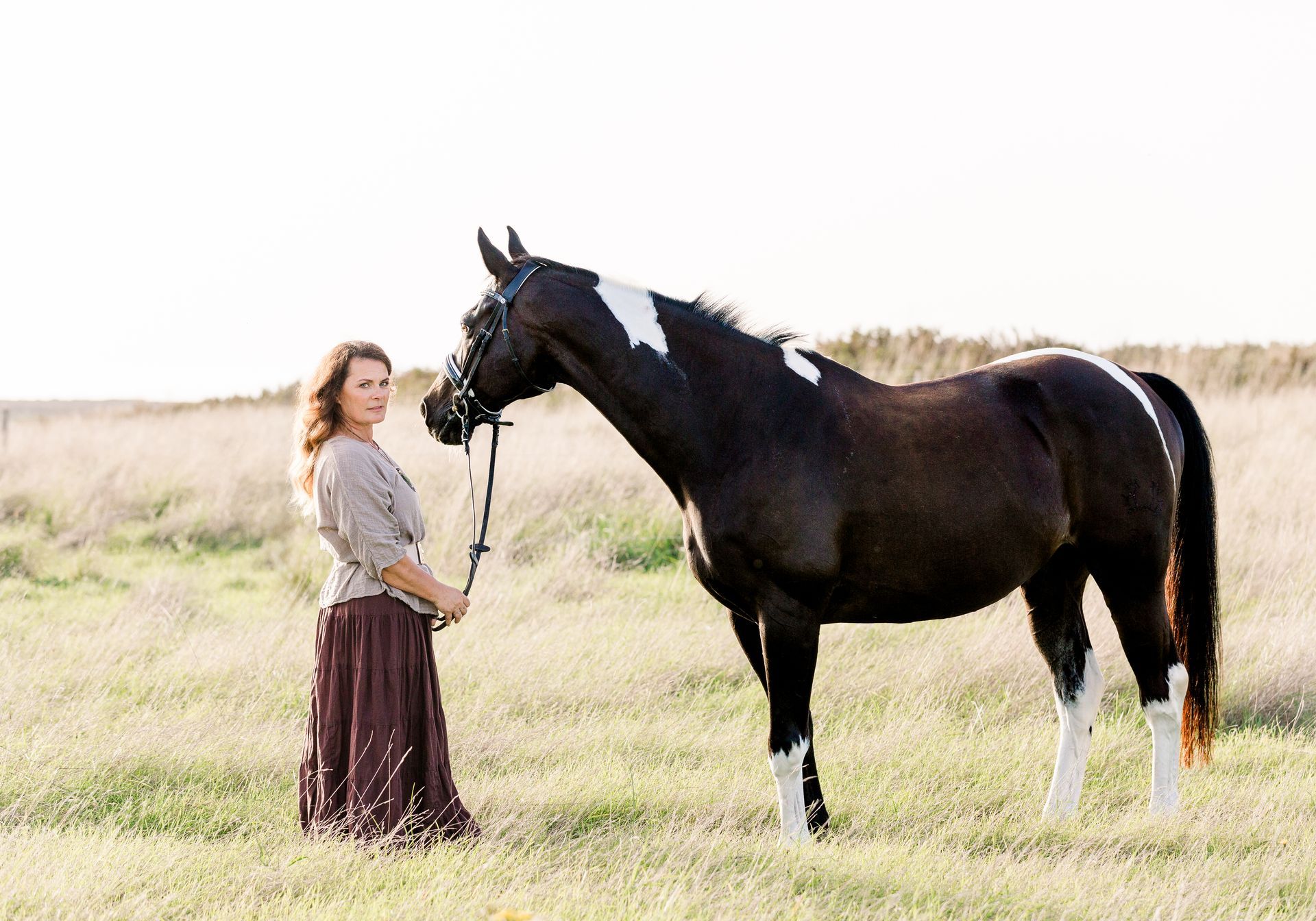 Woman standing next to a black and white horse in a grassy field.