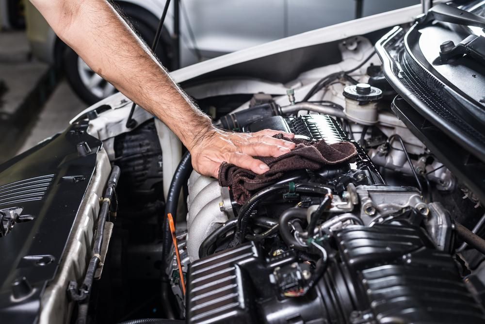 Mechanic cleaning car engine with a cloth, under the open hood.