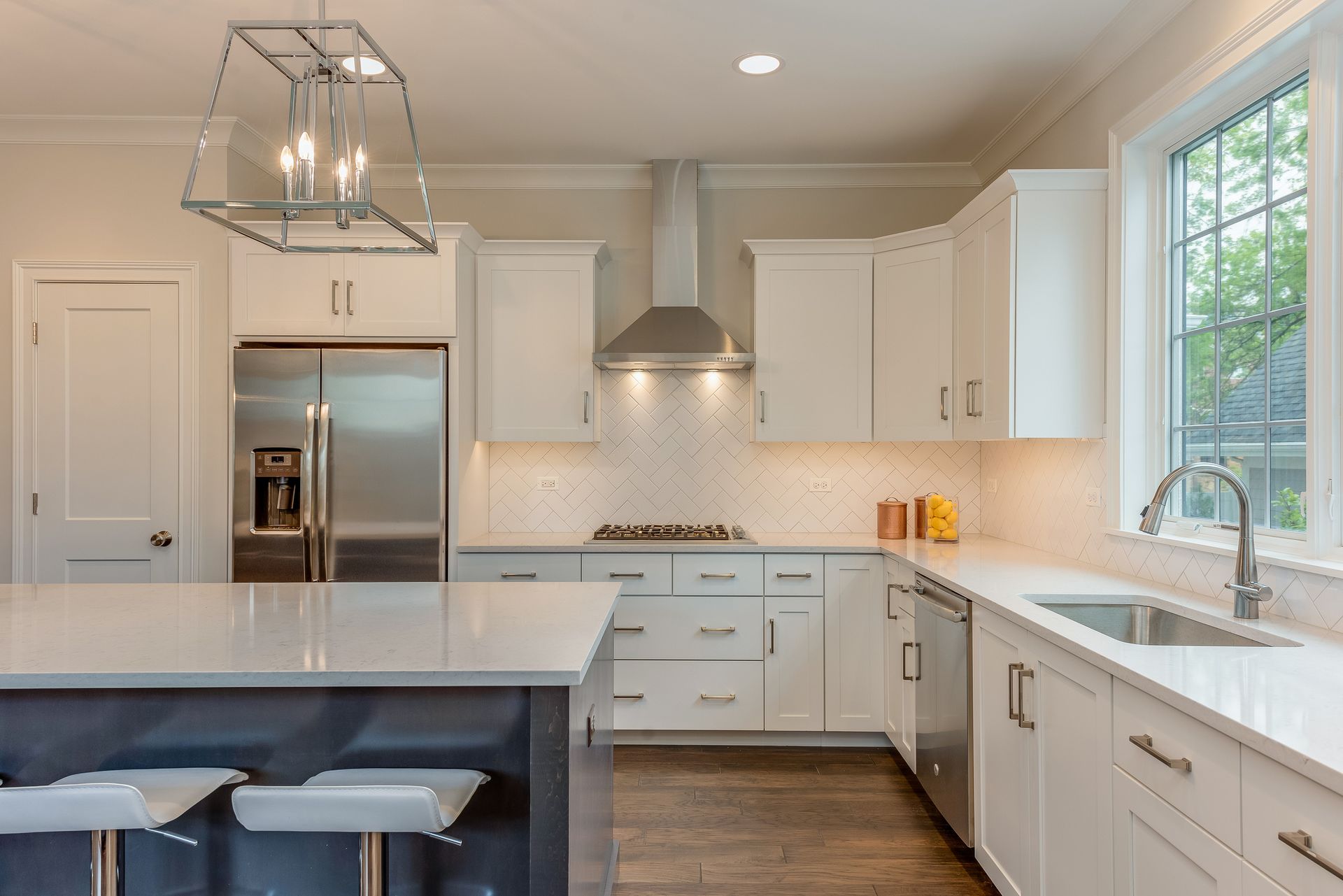Modern white kitchen with stainless steel appliances, island, and window.