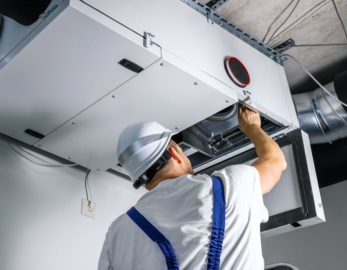 A man wearing a hard hat is working on a ventilation system.