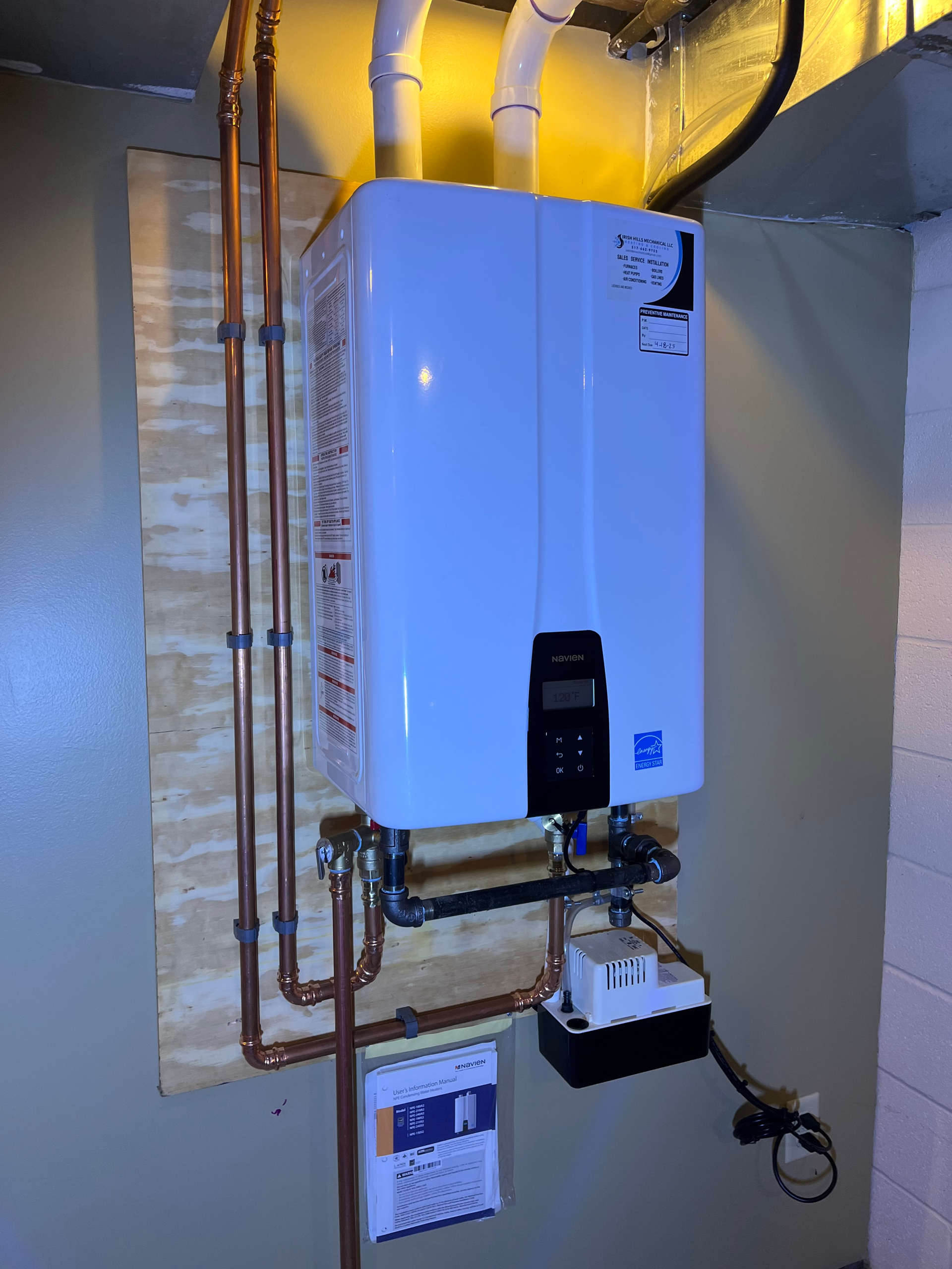 A white water heater is mounted to a wall next to copper pipes