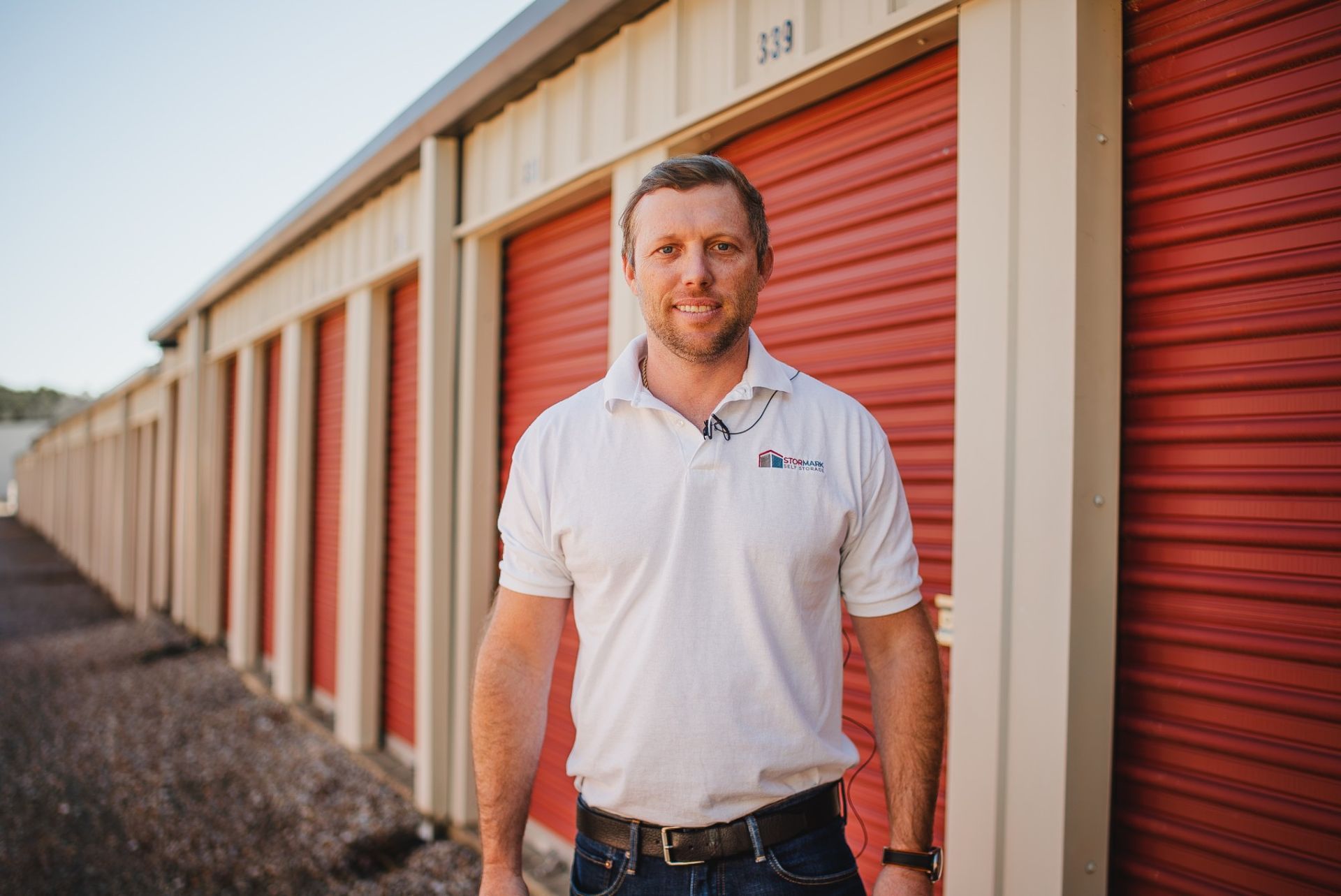 A StorMark team member standing in front of a row of red drive-up storage unit doors