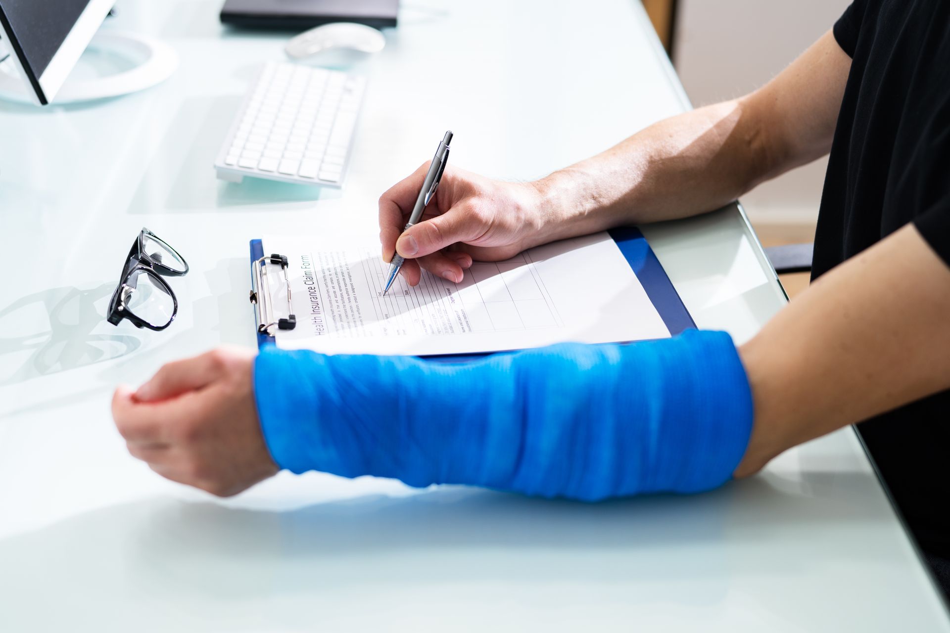 Person with blue cast on arm writes on paperwork at a desk.