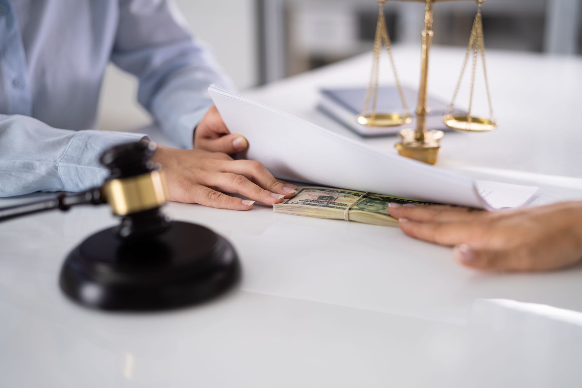 Hands exchanging cash on a desk beside a gavel and scales of justice in a law office