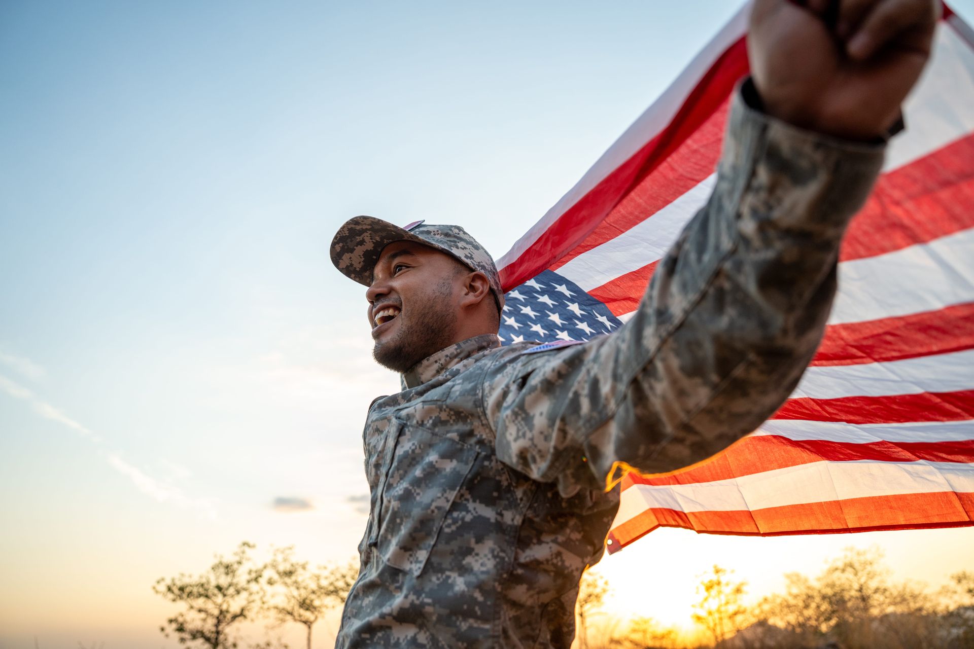Soldier in camouflage holding a waving U.S. flag at sunset