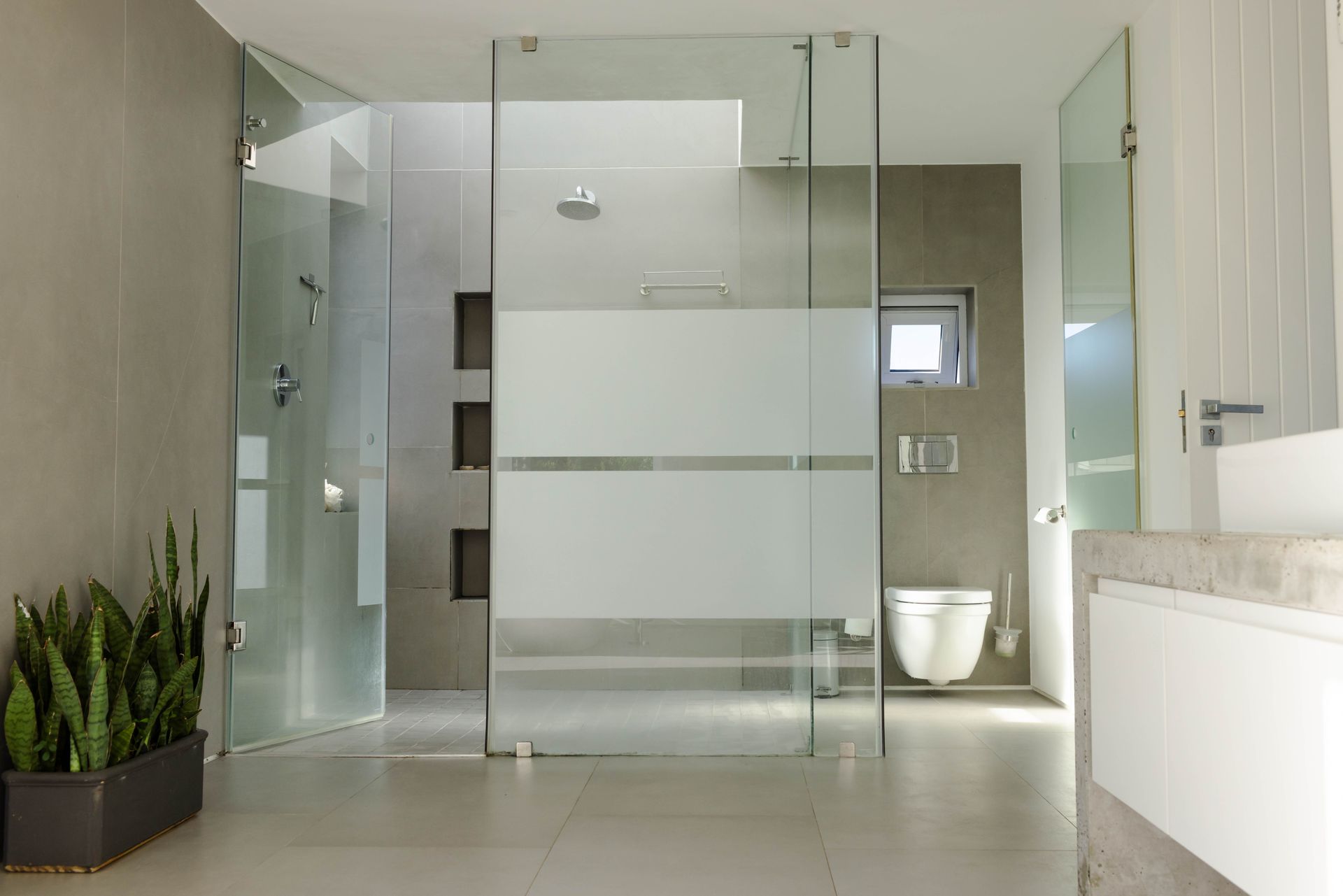 Frameless glass shower enclosure in a modern gray tiled bathroom.