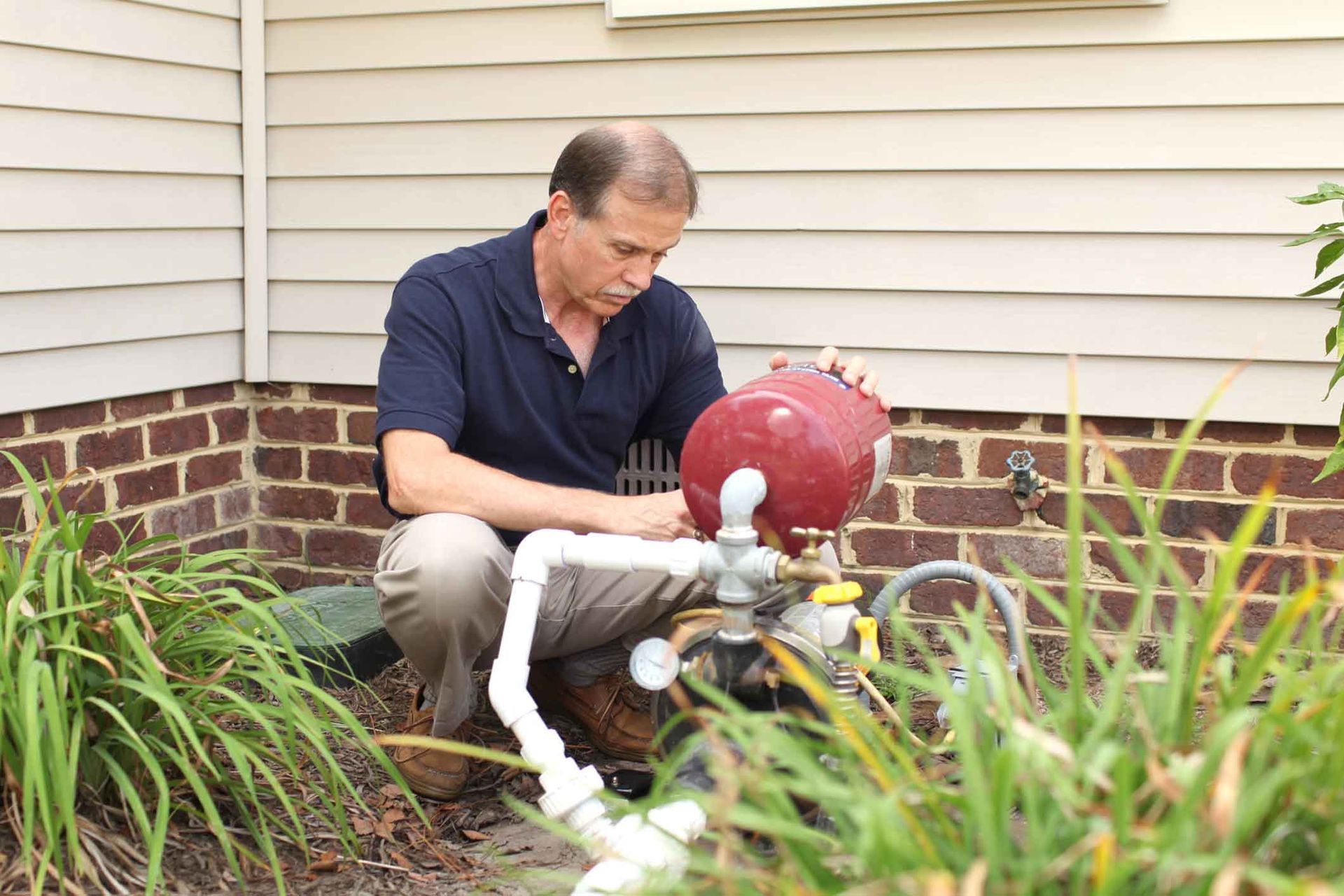 A man is working on a water pump outside of a house.