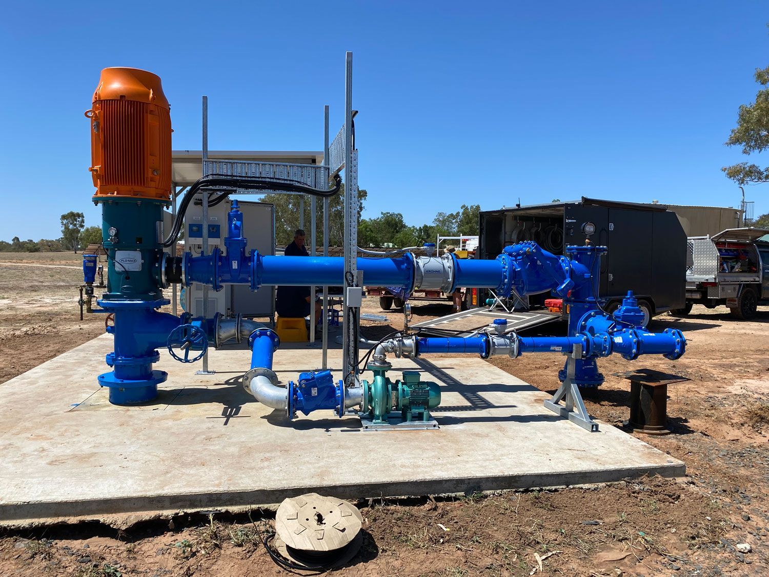 Blue industrial pump and piping system on a concrete pad in an outdoor utility area