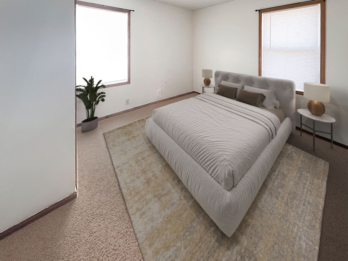 A bedroom with a large bed , two windows , a rug and a plant.
